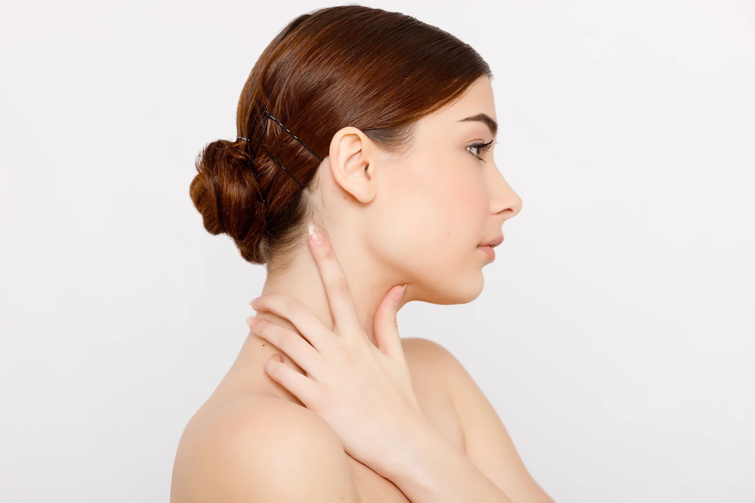 Young woman with smooth, glowing skin touching her neck, showcasing natural beauty and healthy complexion at Unfiltered Medical Spa