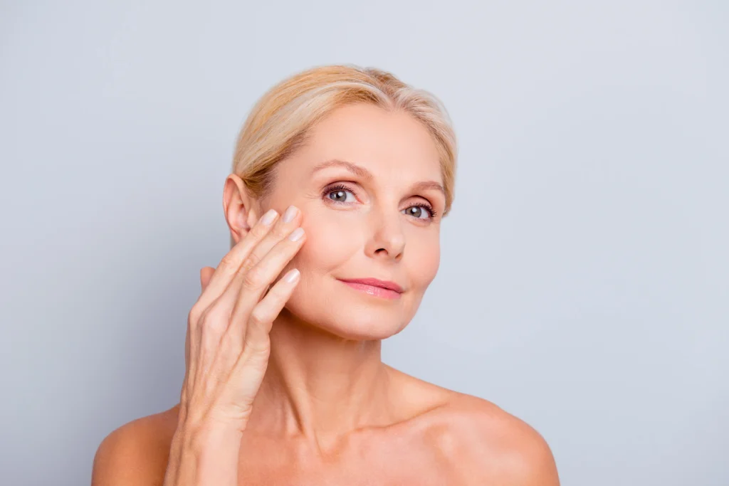 Confident mature woman touching her cheek, showing smooth, youthful skin after aesthetic treatment at Unfiltered Medical Spa